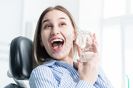 一个快乐迷人的女孩坐在牙科椅上的画像 看牙医时笑着的女孩手里拿着下巴模型图片