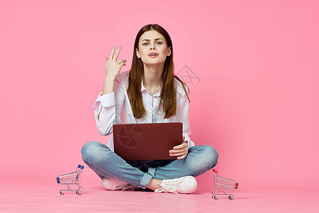 妇女用笔记本电脑坐在地面技术网上购物粉色背景的互联网上女孩信用店铺互联网女性卡片白色电子商务女士房间图片
