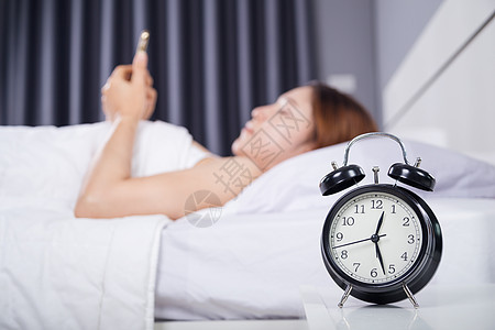 女人在床上用智能手机时钟警报女孩枕头睡眠卧室成人互联网女性时间说谎图片