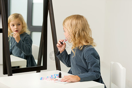 一个小女孩靠近镜子 画着唇唇膏头发孩子乐趣化妆品裙子魅力嘴唇女儿女孩童年图片