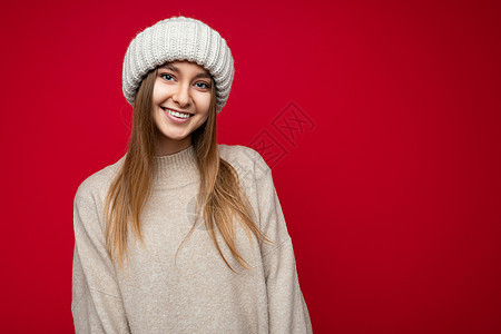 迷人的微笑快乐的年轻深色金发女性孤立地站在色彩缤纷的背景墙上 穿着日常时尚的服装 看着镜头表现出面部情绪喜悦帽子女士毛衣幸福米色图片