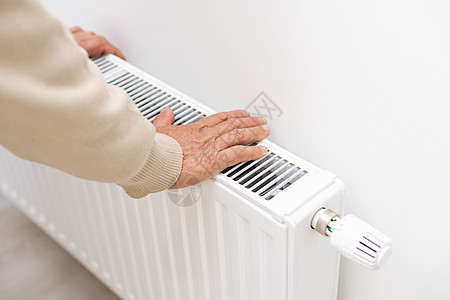 一个老人冻僵在他的手上 一个男人在公寓的暖气片附近暖手 一个男人在公寓里冻僵图片