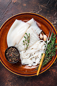 切片生环状鱿鱼 在一个有迷迭香的锈盘子里 深色背景戒指烹饪胡椒香料乌贼管子白色厨房黑色食物图片