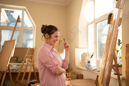 可爱的女人在艺术工作室的画布上作画 艺术家创作图片 艺术学校或工作室 使用颜料 画笔和画架 爱好和休闲的概念 工作区的女画家幸福图片