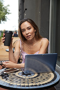 坐在咖啡厅外 拿着笔记本电脑喝着咖啡的年青年轻漂亮女孩饮料咖啡店女士杯子裙子眼镜企业家远程女性手机图片