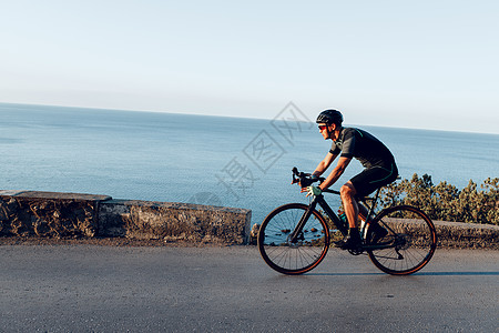 骑在沿海公路上的骑自行车运动运动员太阳镜海岸肌肉男性行动骑士头盔速度男人图片