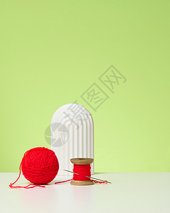 红色球 有羊毛线和大针 在白桌上 绿色背景图片