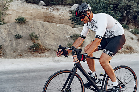 骑单车者在日落的野外公路自行车上行驶行动头盔运动男人骑士男性肌肉太阳镜速度运动员图片