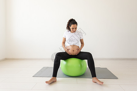 孕妇瑜伽一名年轻孕妇坐在垫子上并抱着肚子时 利用健身球进行放松锻炼活动 (第3条)背景