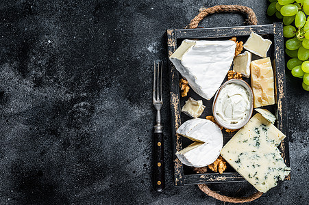 什锦奶酪拼盘 包括布里奶酪 卡门培尔奶酪 羊乳干酪 帕玛森奶酪 蓝奶油奶酪 葡萄和坚果 黑色背景 顶视图 复制空间小吃美食家木板图片