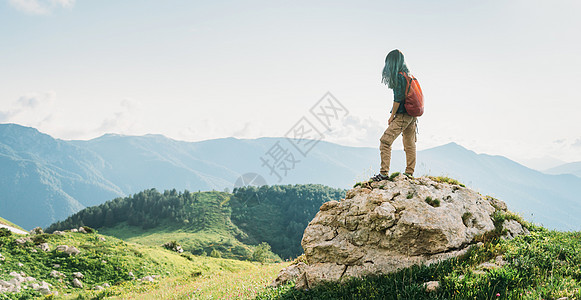 带着背包的年轻女人 站在夏季山里的岩石石上 看着远处 望着距离图片
