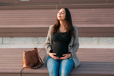 积极的怀孕概念 快乐的年轻企业或学生孕妇坐在长凳上 未来的妈妈在怀孕后期工作或学习图片