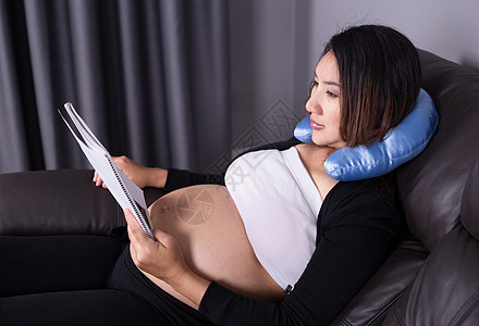 躺在沙发上和阅读书上的孕妇怀孕父母说谎房间休息生活长椅脖子微笑成人图片
