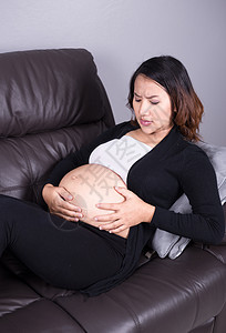 孕妇在起居室收缩的怀孕妇女压力成人房间腹部女性长椅母亲房子家庭疾病图片