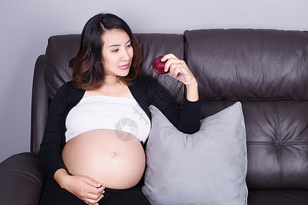 孕妇饮食孕妇在沙发上在家用红苹果休息家庭房间饮食食物肚子妈妈婴儿女性微笑成人背景