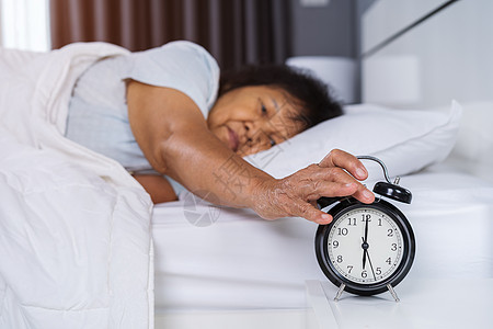 睡在床上的高级女人 按着清晨闹钟时的按声按钮退休成人苏醒睡眠压力女性就寝时间枕头休息图片