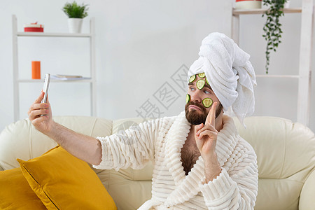 长胡子的可爱男人拿着黄瓜切片脸部 在家里 身体和皮肤上照顾男性概念面具产品奶油化妆品美容师毛巾奢华润肤保湿美容图片