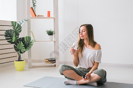 年轻美丽的女孩在垫子上练瑜伽 休息时喝着饮用水 健康 健康的生活方式概念运动装女性瓶子有氧运动房间力量运动动机培训师运动员图片