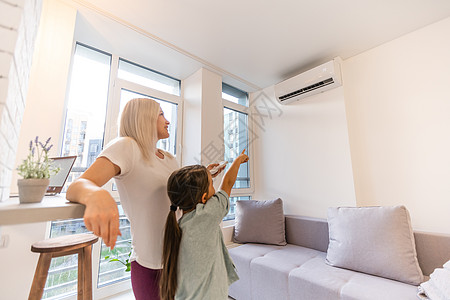 吹空调女孩空调下的幸福家庭 妈妈拿着客厅空调的遥控开关 为女儿调节舒适温度 现代家庭的气候系统背景