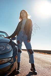 身穿皮夹克的无屋顶汽车附近的年轻妇女皮革晴天太阳自由外套车辆乐趣蓝色驾驶微笑图片
