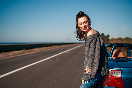 在无屋顶汽车露天附近站着尾巴的年轻女子天空乐趣旅行自由阳光蓝色海滨车辆太阳沙漠图片