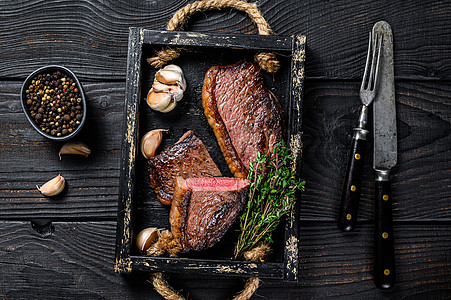 木制托盘中的烧烤烤臀盖或巴西 picanha 牛肉牛排 黑色的木制背景 顶视图炙烤大理石纹牛肉食物鱼片胡椒桌子红色迷迭香木板图片