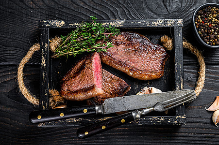 木制托盘中的烧烤烤臀盖或巴西 picanha 牛肉牛排 黑色的木制背景 顶视图草本植物炙烤香料迷迭香牛扒木板大理石纹红色胡椒桌子图片