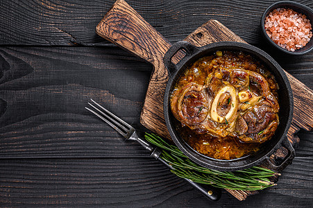 炖小牛肉小腿肉 OssoBuco 意大利 osso buco 牛排 黑色的木制背景 顶视图 复制空间迷迭香棕色午餐蔬菜香料食物红图片