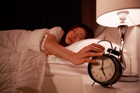 睡在床上 眼睛闭着的困睡妇女 清晨将手伸向闹钟女士唤醒休息房子枕头睡眠女性成人苏醒时间图片
