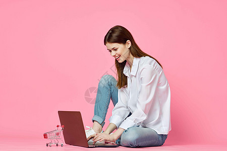 妇女坐在地板上 手持笔记本的在线购物技术粉红色背景信用商业粉色电脑夫妻房间电子商务女性地面银行业图片