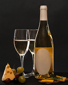 在黑色背景中 一瓶白葡萄酒 两杯白葡萄酒 旁边是葡萄 一块三角形奶酪 一个三明治配奶酪和香草图片