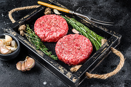 木制板上的肉和草药 作为汉堡的生牛肉肉饼 黑色背景 顶层视图图片