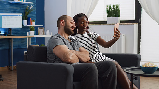 使用智能手机视频电话的跨种族伙伴会议男人妻子沙发长椅成人男朋友女士互联网丈夫图片