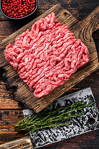 Raw mince牛肉 土肉以及木制切割板上的草药和香料 黑木背景肉馅胡椒羊肉地面猪肉烹饪大理石纹红色食物迷迭香图片