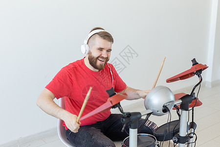 人 音乐和爱好概念     穿红色T恤衫的人在电子鼓架上玩娱乐工具成套男人鸡腿喜悦衬衫耳机乐器成人背景图片