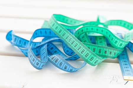 放在桌上的紧闭蓝色和绿色计量带 健康饮食和体重减肥的概念衡量标准;在表格中图片
