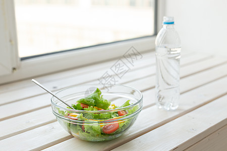 白色窗台上放着蔬菜沙拉和一瓶水 健康生活方式体育活动和适当营养的概念图片