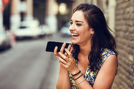 微笑的年轻女子 在她的智能手机里录音语音音符城市裙子女孩技术棕色头发休闲服女性成人卷发图片