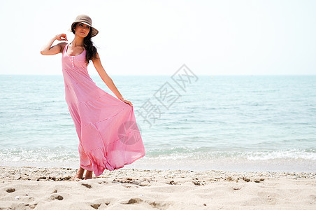 在热带沙滩上穿长着粉红裙子的漂亮女人棕褐色女孩旅行海浪海岸阳光季节牙裔假期发型图片