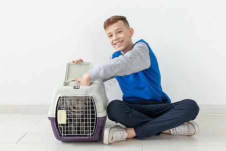 笑笑的男孩拿着一个笼子和一只苏格兰折叠猫坐在他旁边 坐在新公寓的地板上 保护宠物的概念婴儿工作室毛皮哺乳动物眼睛尾巴小猫乐趣折叠图片