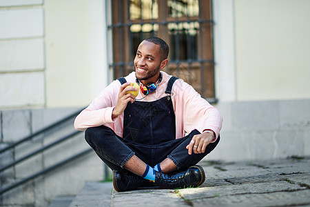黑人年轻人坐在城市的阶梯上吃苹果男性快乐街道成人衣服毛衣健康水果黑色胡须图片