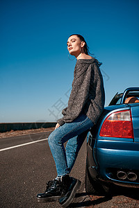 在无屋顶汽车露天附近站着尾巴的年轻女子天空乐趣微笑自由晴天车辆海滨太阳驾驶蓝色图片