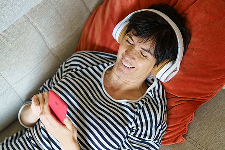 女人笑着看着她的智能手机 同时用耳机听音乐 (笑声)图片