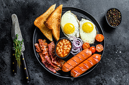 英语早餐 炸鸡蛋 香肠 培根 豆子和烤面包在盘子里 黑色背景图片