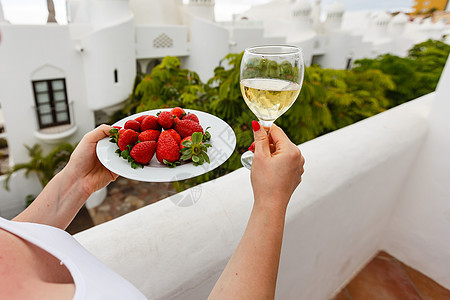 女人在阳台上吃着新鲜的红草莓水果叶子女性太阳甜点成人浆果咖啡女孩食物图片