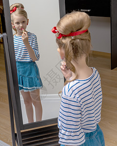 一个小女孩靠近镜子 画着唇唇膏裙子喜悦童年乐趣孩子头发魅力快乐眼睛女性图片