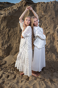 两个有魅力的年轻姐妹 穿着优雅白色衣服 在采沙场上摆着高雅白衣姐姐夹克女士沙坑金发女郎长发手电筒冒充金发双胞胎图片