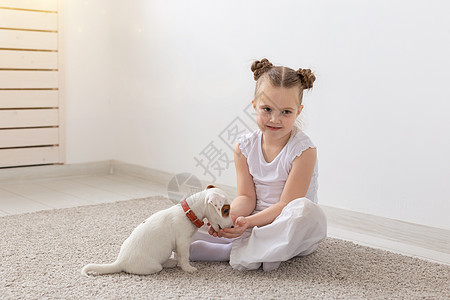 宝宝和狗儿童 宠物和动物的概念  穿着睡衣的小女孩在地板上和杰克罗素梗犬玩耍沙发孩子婴儿友谊房子放松女儿微笑小狗生活背景