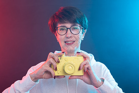 摄影师 艺术和爱好概念     50岁的妇女将黄色古董相机放在彩色背景上的手掌中粉色指甲女士紫色阴影眼镜眼皮棕色乐趣头发图片