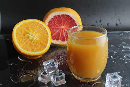 杯子里的橙色咸黄汁 旁边是半份橙子和葡萄果冰 在黑色背景上 清新饮料夏天图片